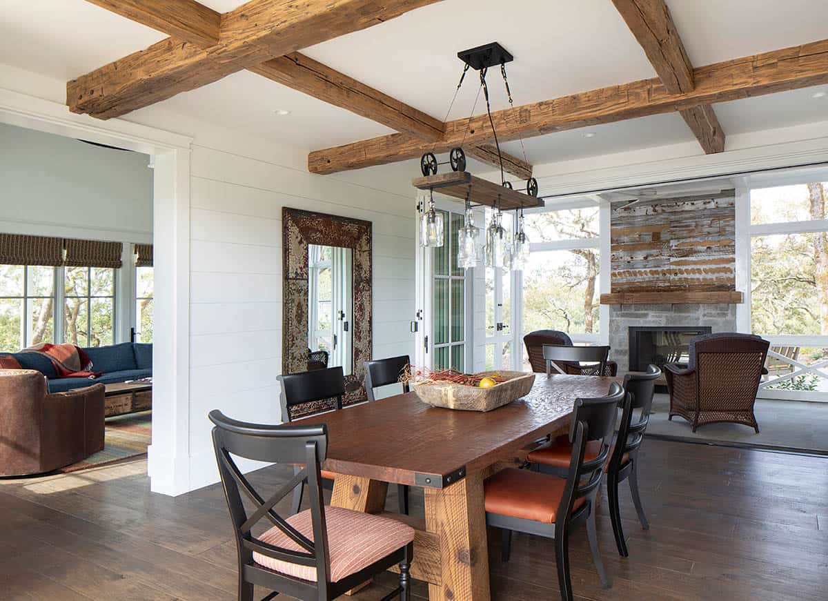 Dining area with reclaimed wood table, industrial pulley chandelier, and stone fireplace beyond