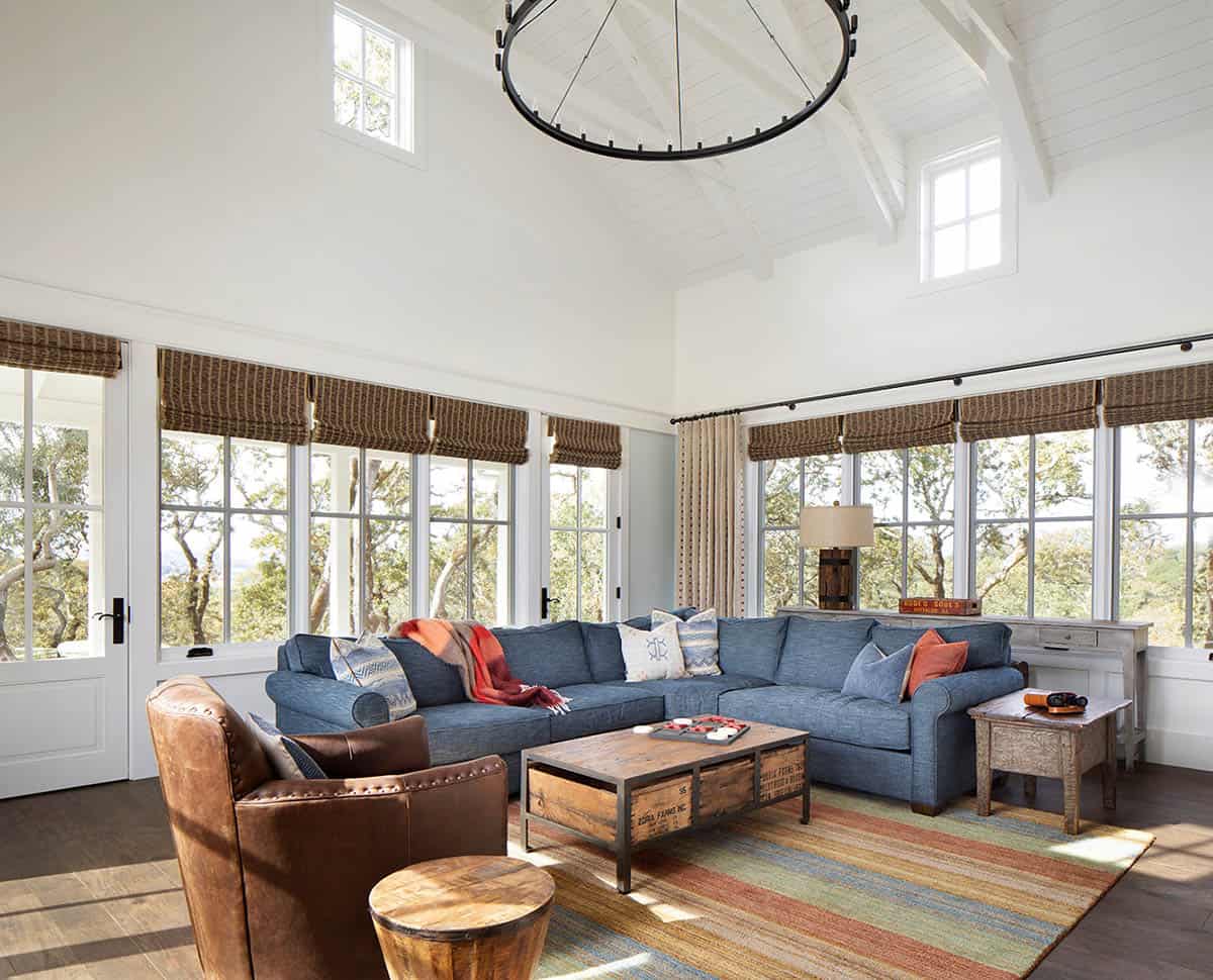 Living room with vaulted ceiling, wagon-wheel chandelier, blue sectional, and large windows
