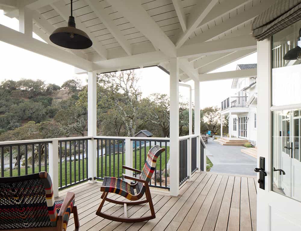 Covered wraparound porch with rocking chairs overlooking the hillside and pool