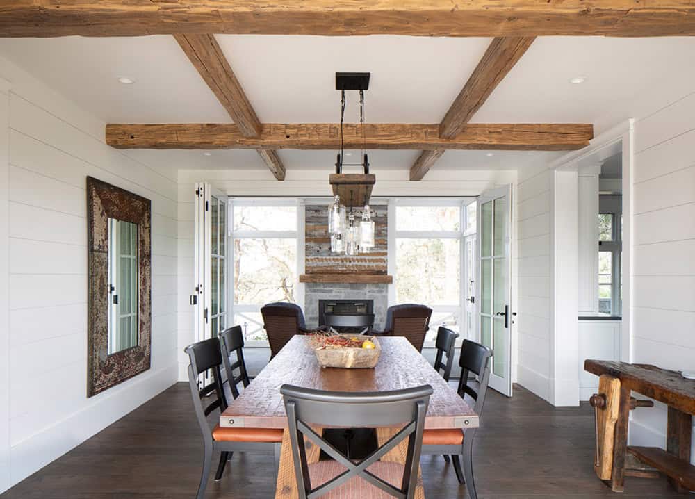 Dining room with reclaimed wood beams, stone fireplace, and French doors to a screened porch