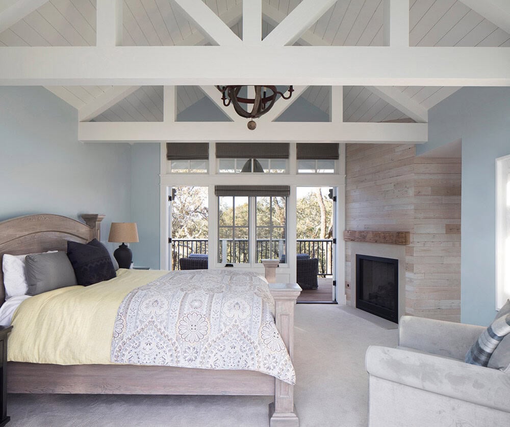 Primary bedroom with exposed truss ceiling, reclaimed wood fireplace wall, and lounge seating