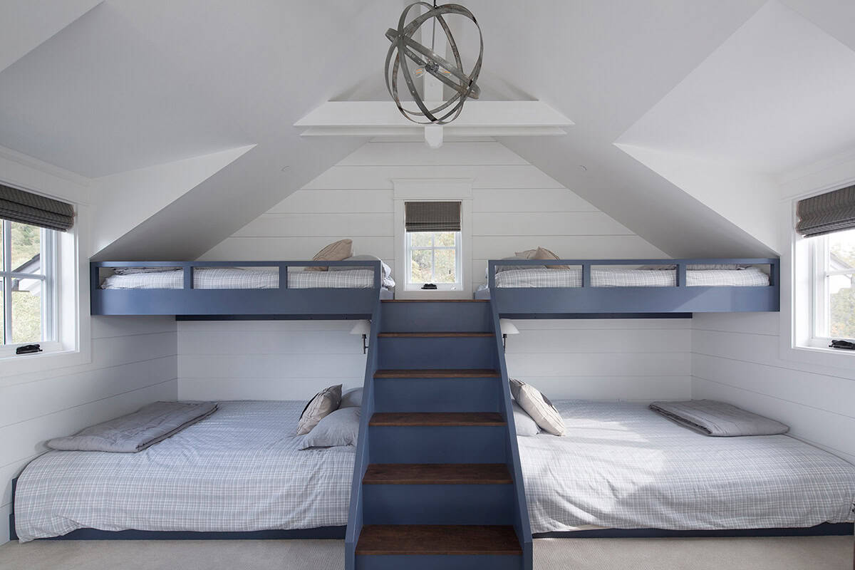 Built-in bunk room with navy blue triple bunks and center staircase under a vaulted ceiling