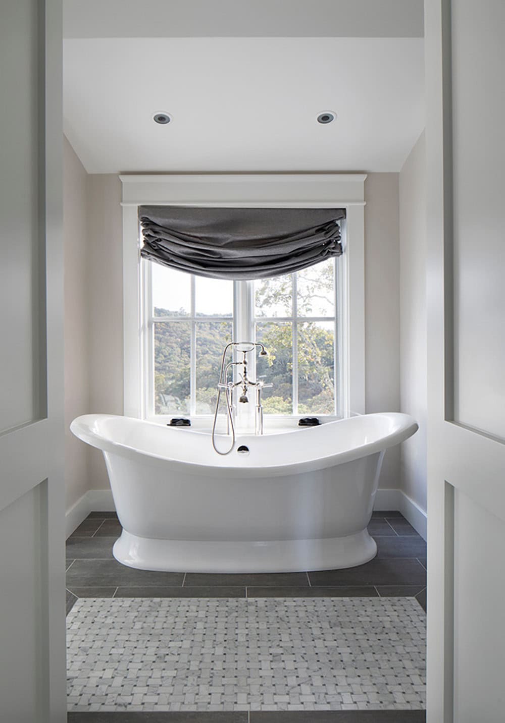 Freestanding tub framed by an open doorway, with window view and marble mosaic floor