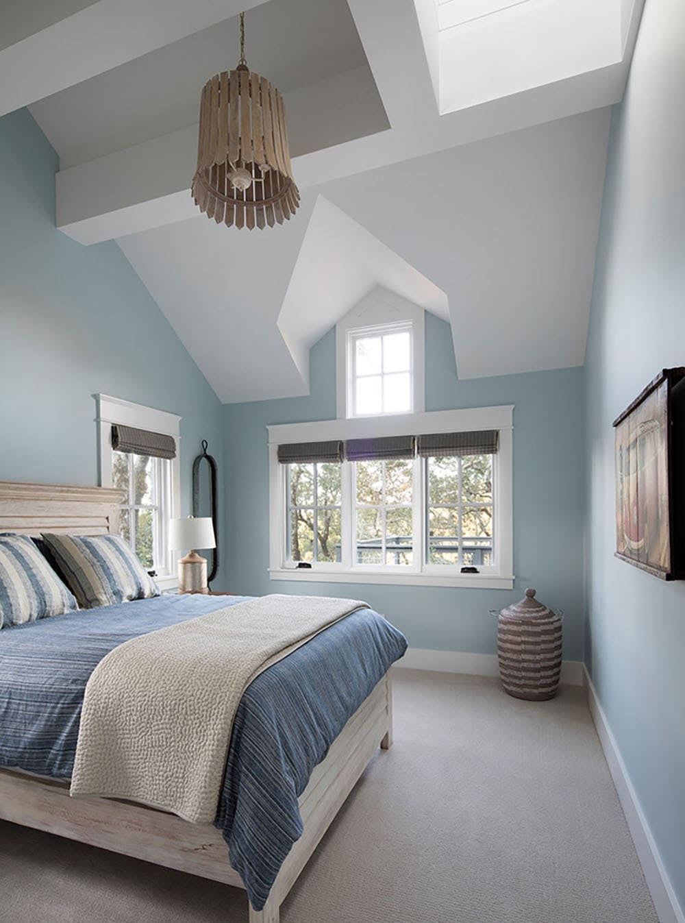 Blue guest bedroom with vaulted ceiling, skylight, and woven pendant light