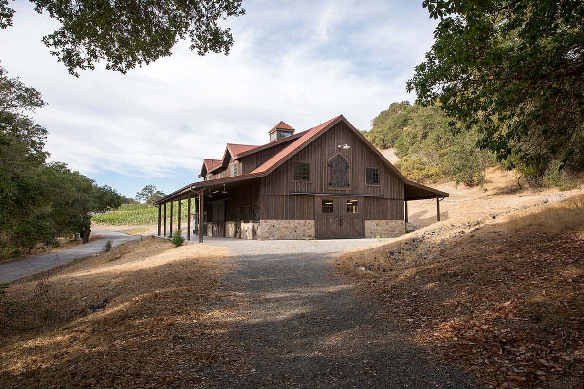 Rustic wood barn with red metal roof, stone base, and covered side porch