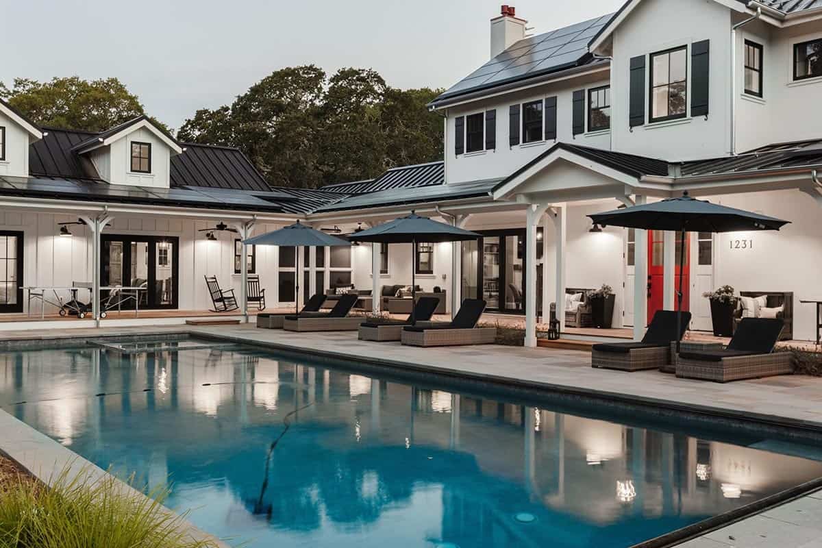 Rear view of farmhouse with covered patio, navy umbrellas, and lounge chairs by the pool