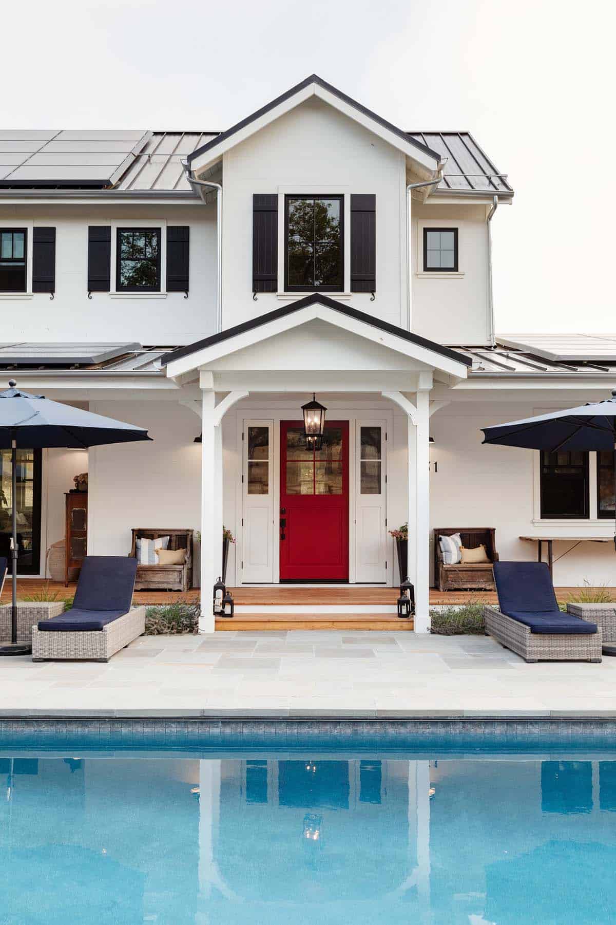 Front porch with red door, gable roof, and poolside lounge chairs