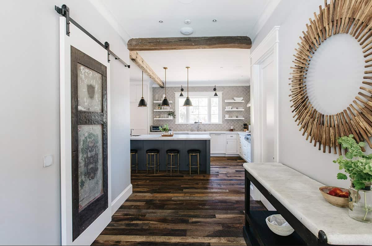 Hallway view into kitchen with sliding barn door and round wood starburst mirror