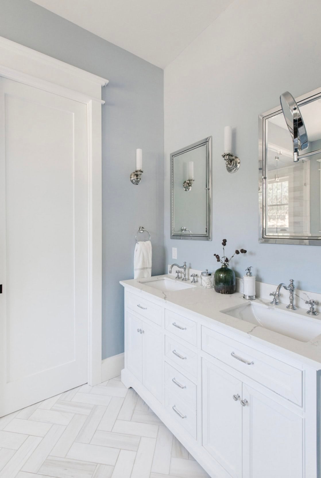 Bathroom double vanity with white cabinets, marble countertop, and herringbone tile floor