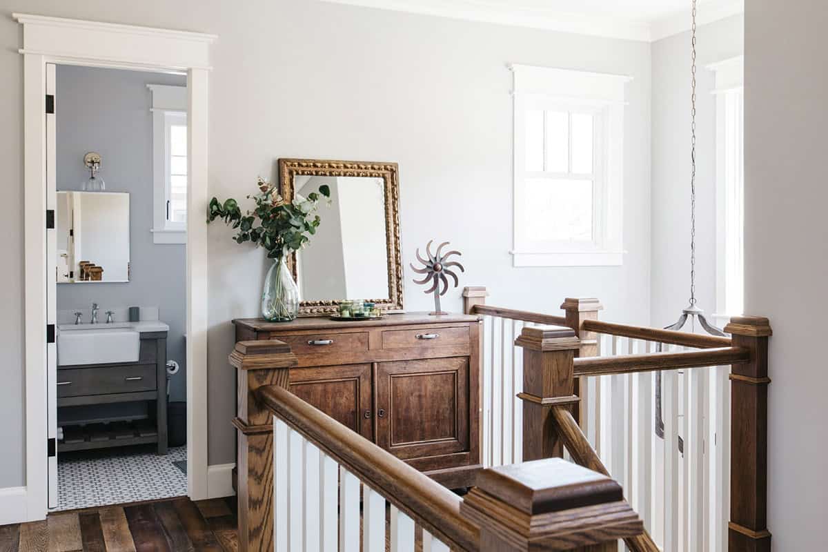 Upstairs landing with antique wood dresser, gilded mirror, and staircase railing