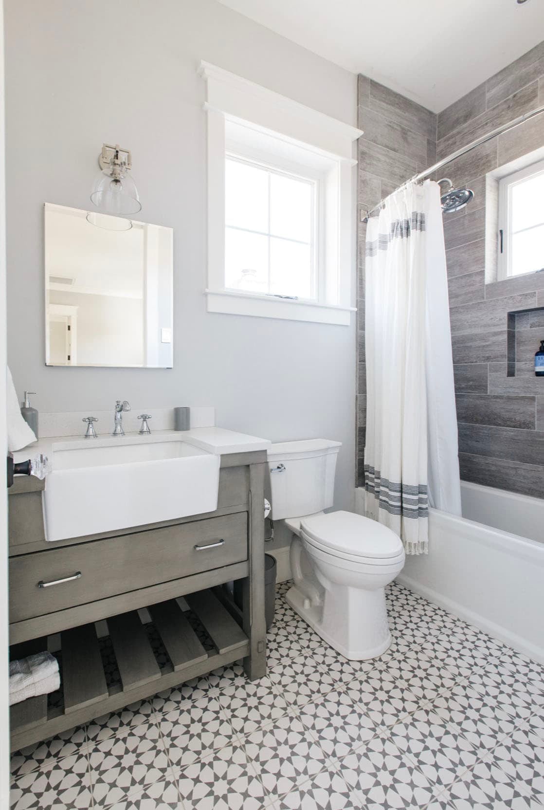 Bathroom with farmhouse sink vanity, wood-look tile shower surround, and patterned floor tile