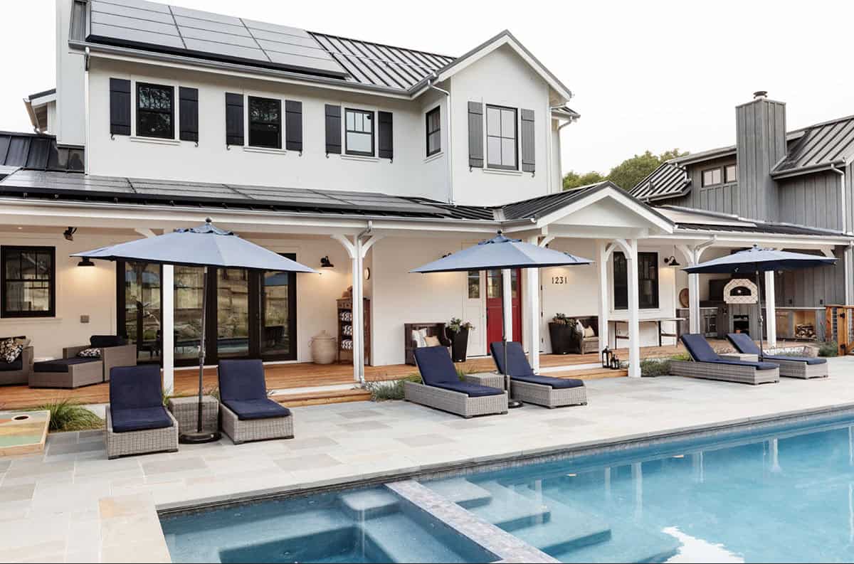 Rear exterior of farmhouse with solar panels, covered porch, and pool with spa