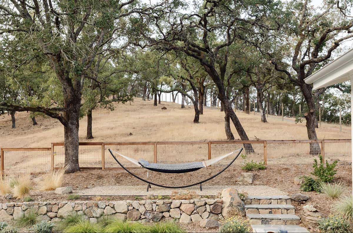 Hammock strung between trees on a hillside with stone retaining wall