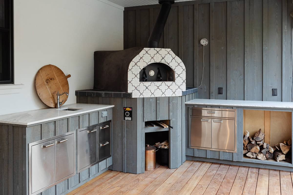 Outdoor kitchen with wood-fired pizza oven, stainless appliances, and stone counters