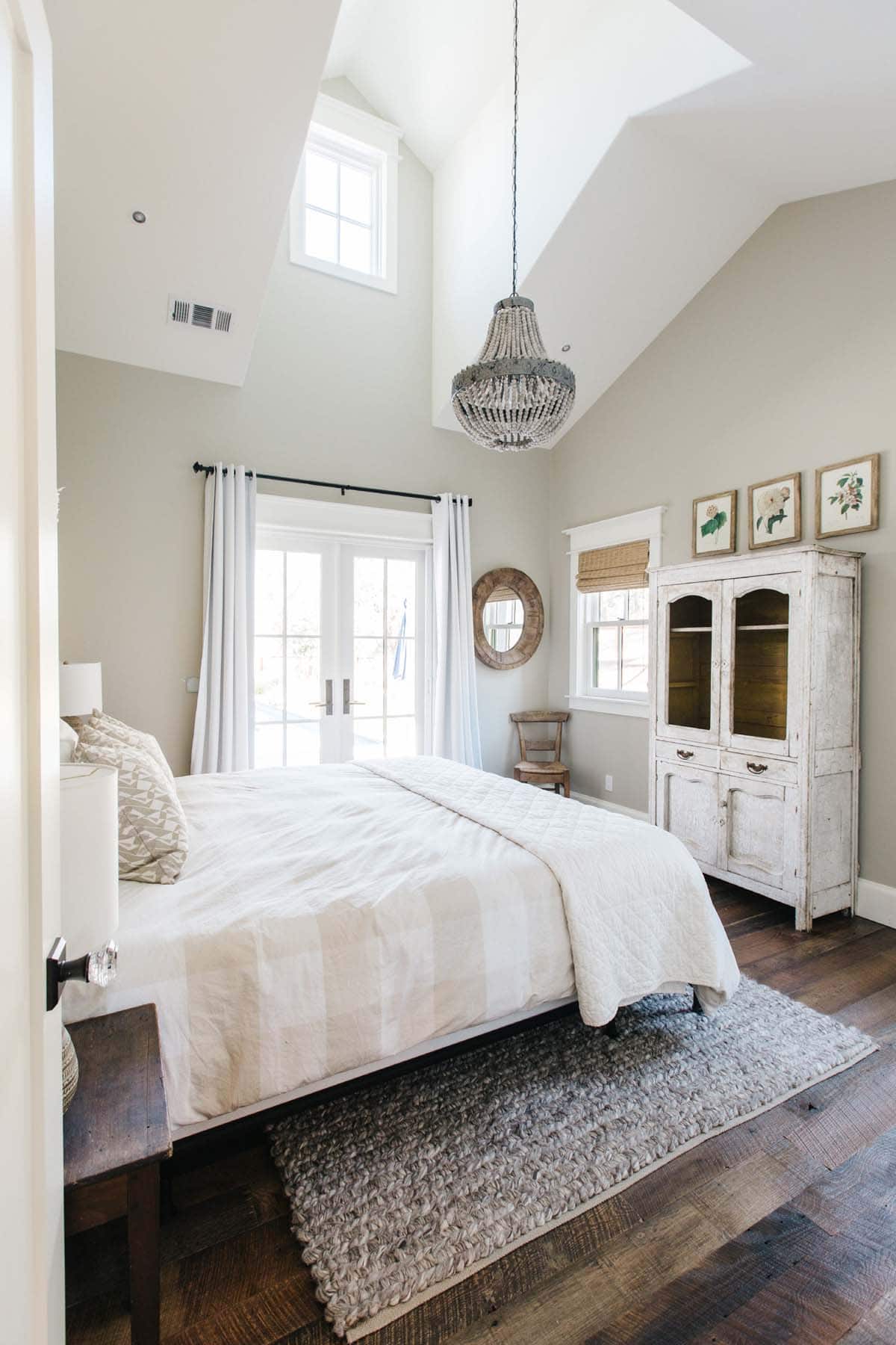 Vaulted bedroom with beaded chandelier, antique cabinet, and French doors