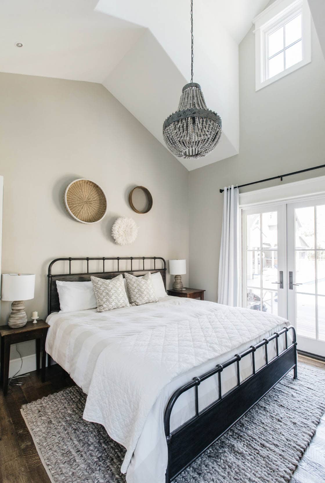 Bedroom with black metal bed frame, beaded chandelier, and wall-mounted baskets