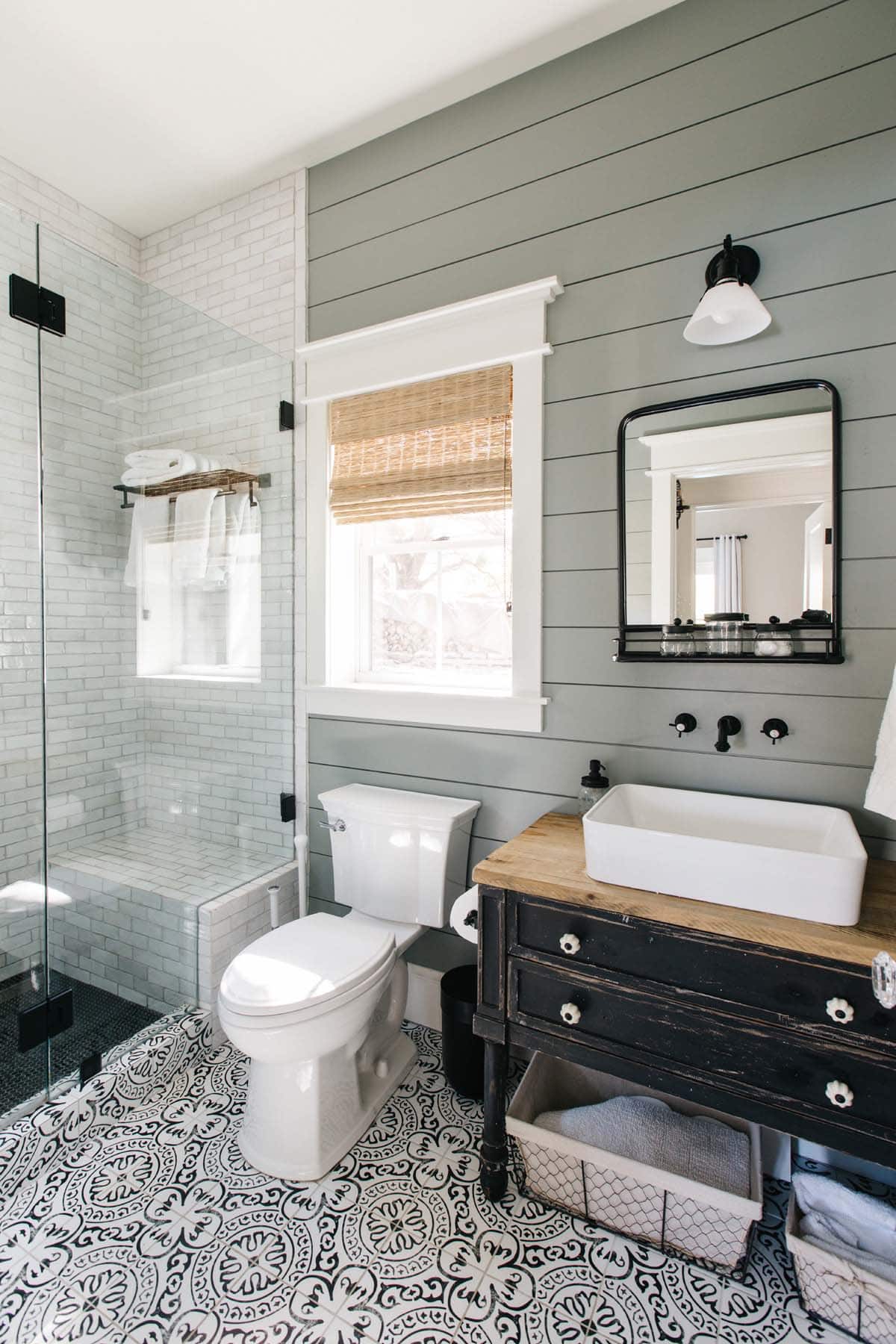 Bathroom with shiplap accent wall, black-framed mirror, and patterned tile floor