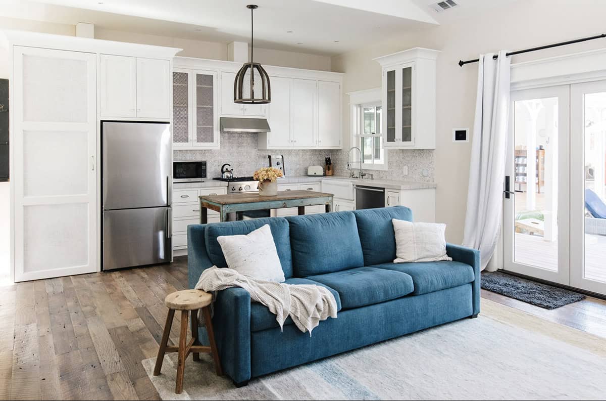 Guest cottage living area with blue sofa, wood-plank floors, and view into kitchen