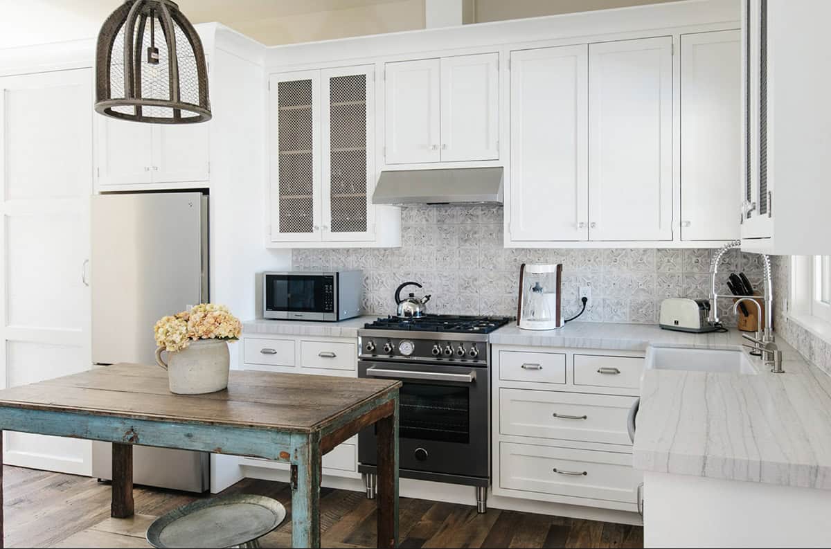 Guest cottage kitchen with white cabinets, mesh-front doors, and rustic wood table