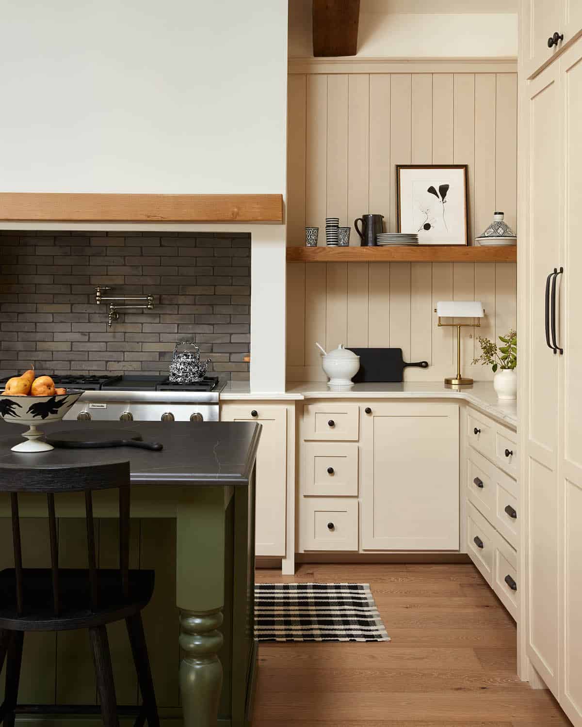 Cream shaker cabinets with brass pot rail beside gas range