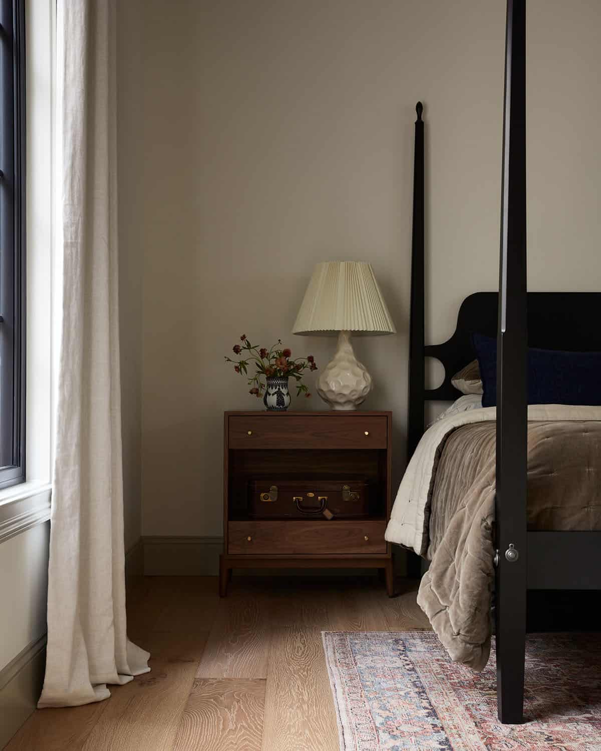 Walnut nightstand and pleated lamp beside black bed post