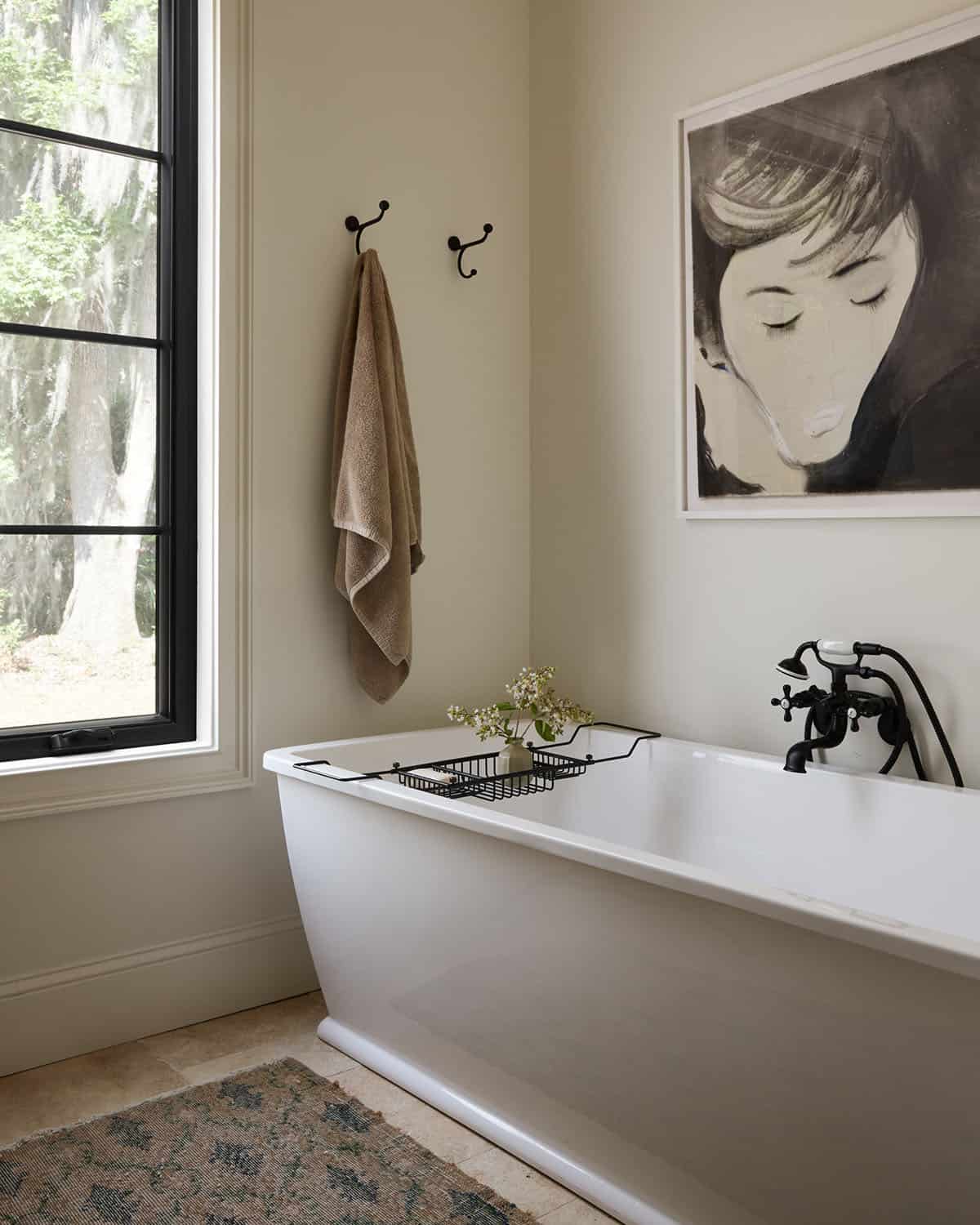 Freestanding tub beneath framed portrait near black steel window