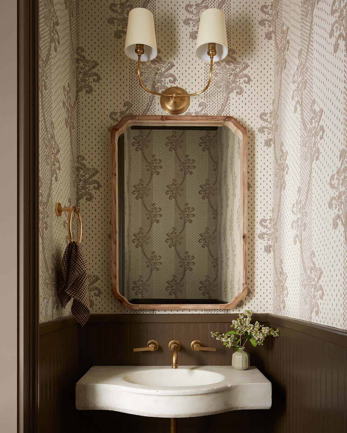Powder room sink with brass fixtures and floral wallpaper