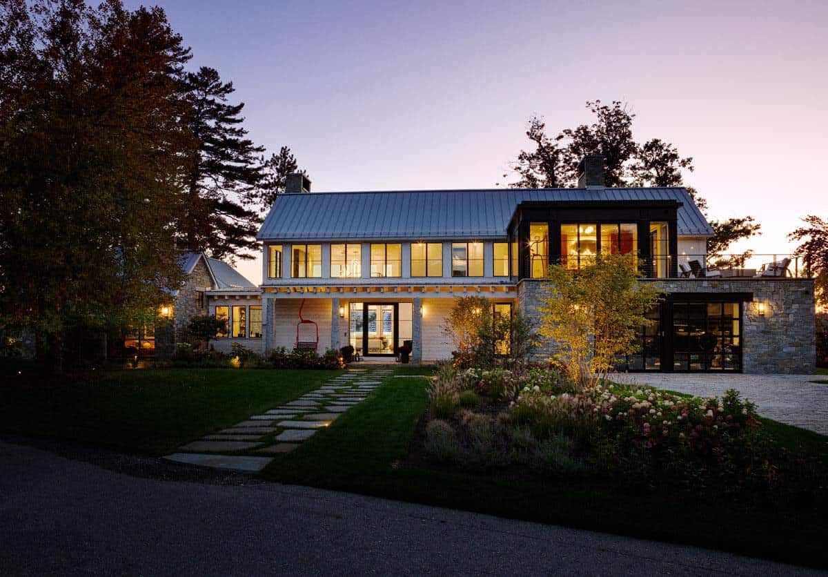 Dusk exterior view of shingle-style lake house with lit interior