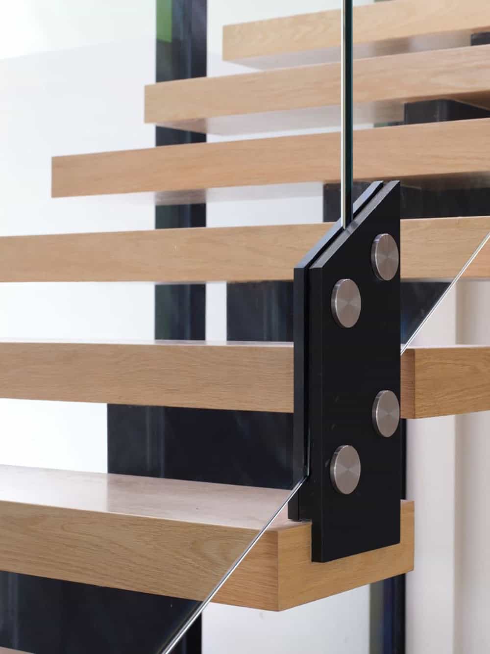 Close-up of black steel bracket connecting wood stair treads to glass railing