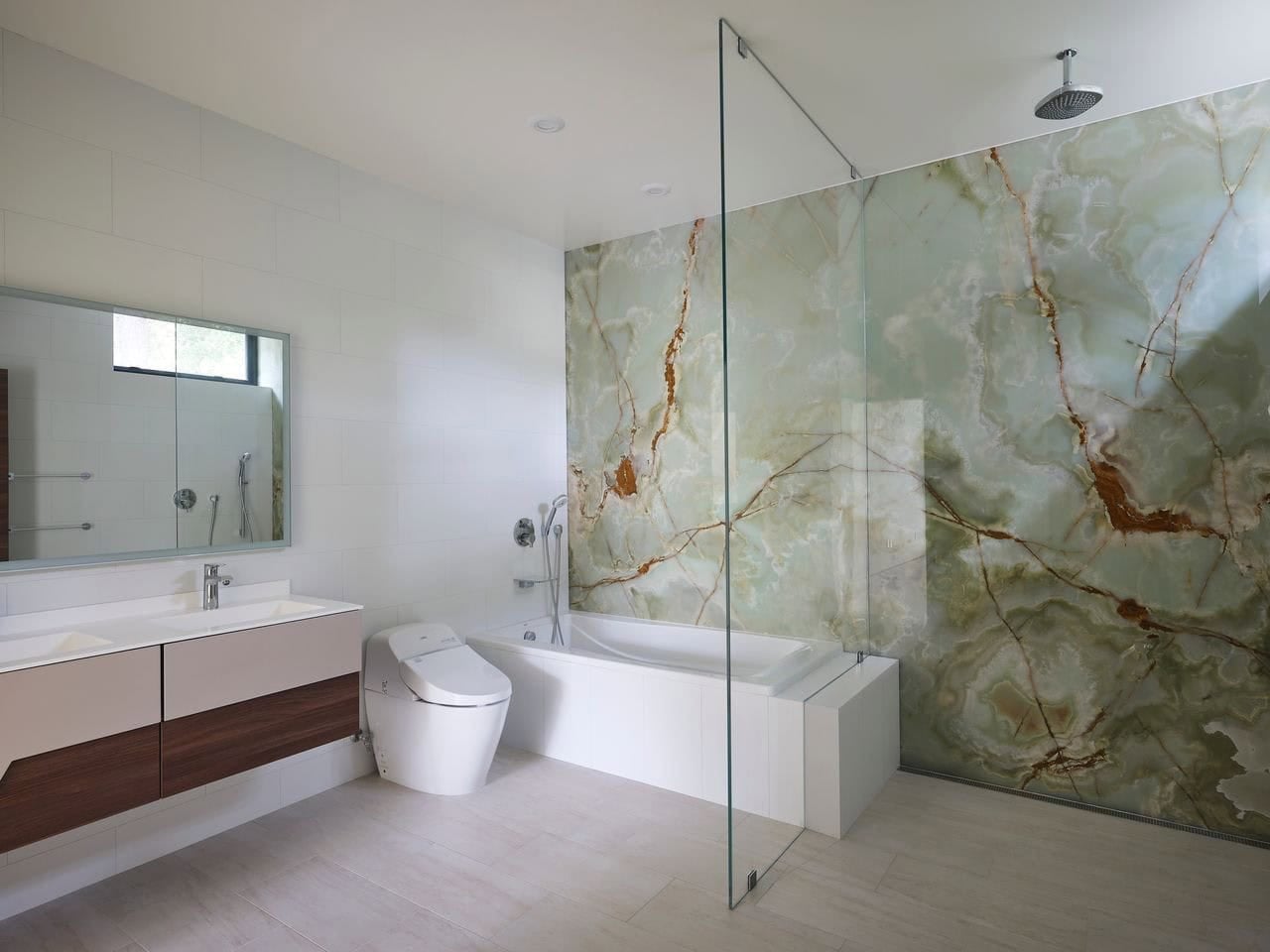 Bathroom with green onyx stone accent wall and glass-enclosed tub