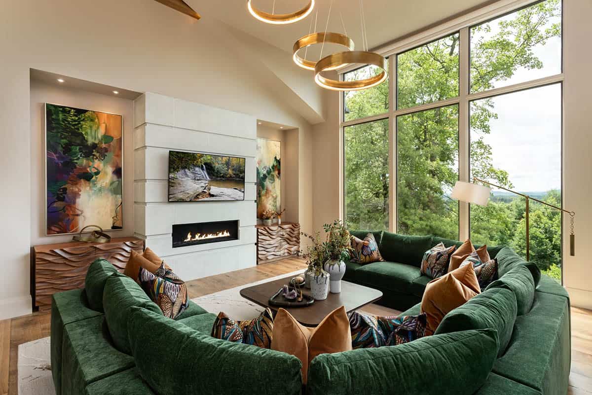 Vaulted living room with green sectional and floor to ceiling forest views