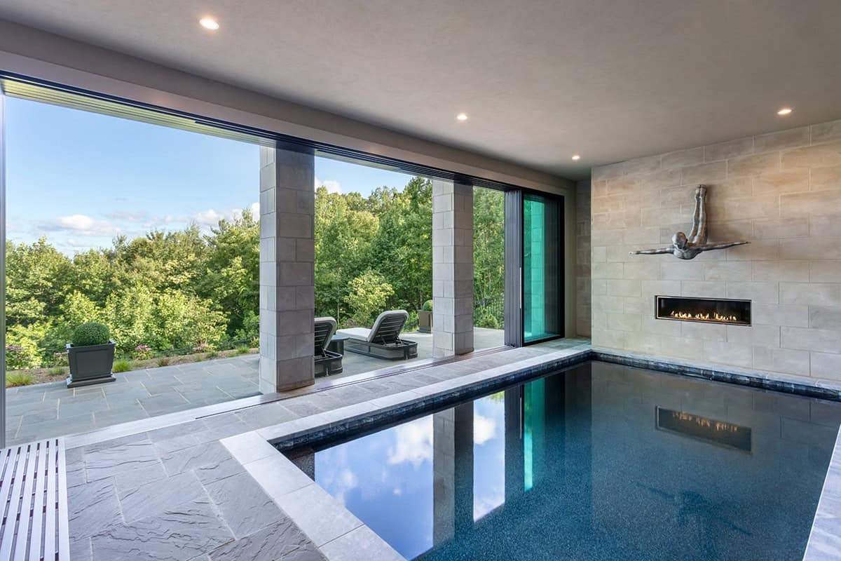 Indoor pool with linear fireplace and folding glass wall to patio