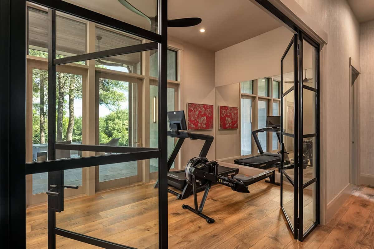 Home gym with black steel doors and dual treadmills facing wooded view