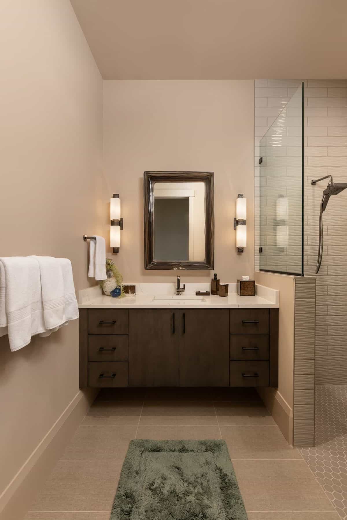 Guest bathroom vanity with carved wood mirror and glass tile shower wall