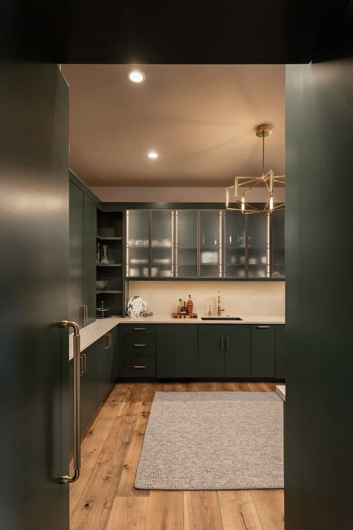 Green cabinetry walk-in pantry with frosted glass uppers and brass chandelier
