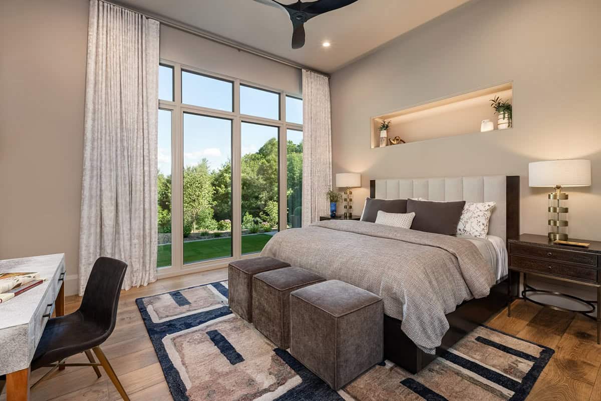 Guest bedroom with tall windows, stacked ottomans, and blue patterned rug