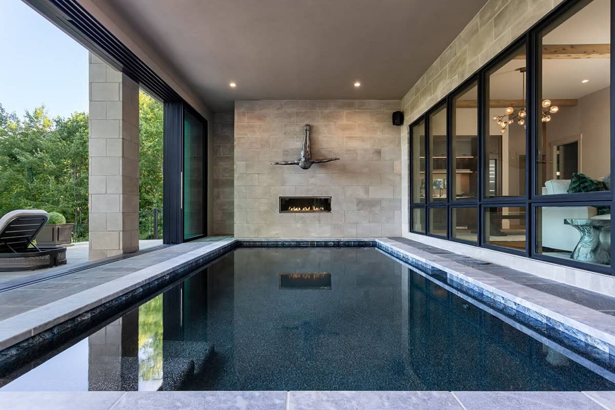 Indoor lap pool beneath diving sculpture with view to wooded patio