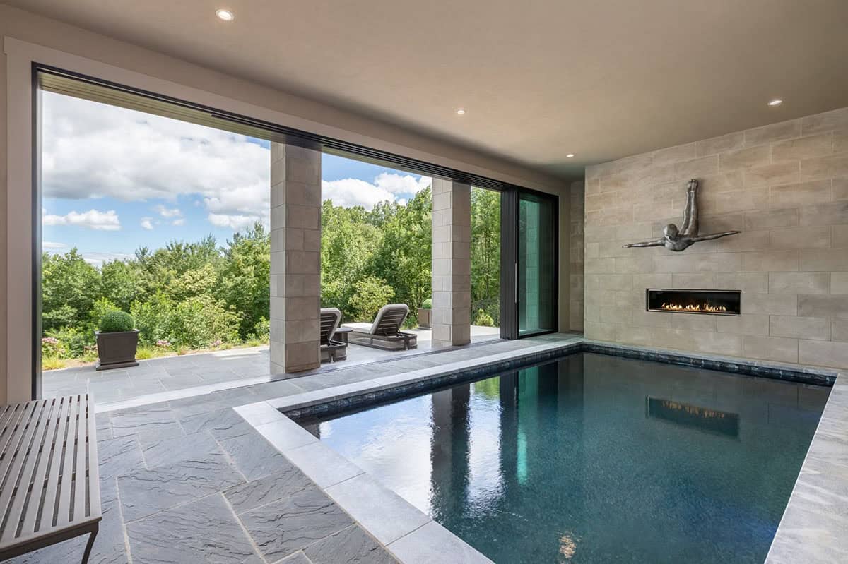 Indoor pool room with stone fireplace wall and folding glass doors