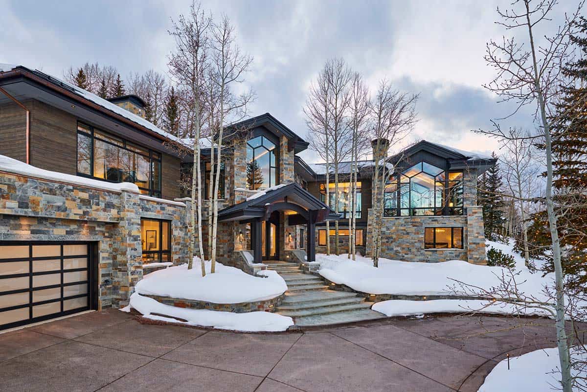 Modern mountain home exterior with stone facade, dark timber accents, and snow-covered landscaping