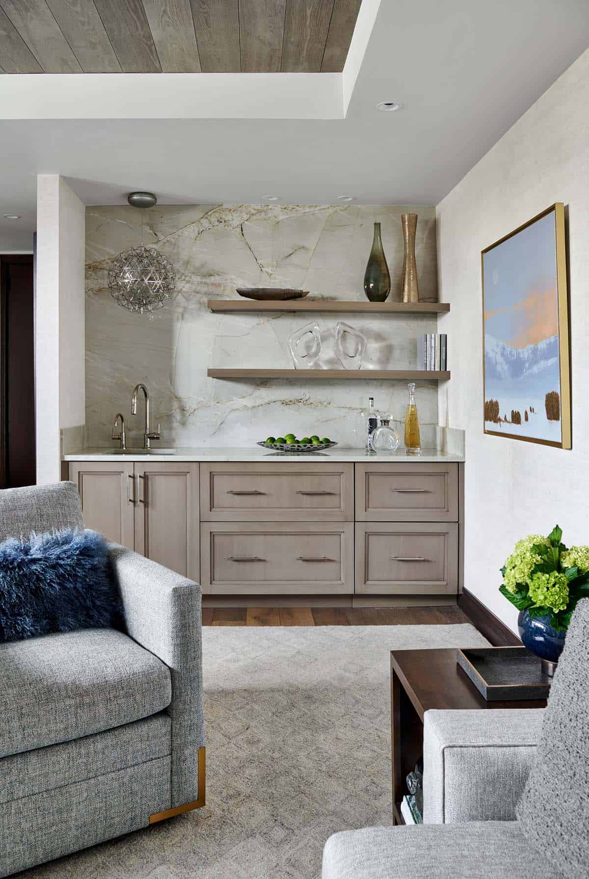Wet bar with marble backsplash, floating wood shelves, and taupe cabinetry