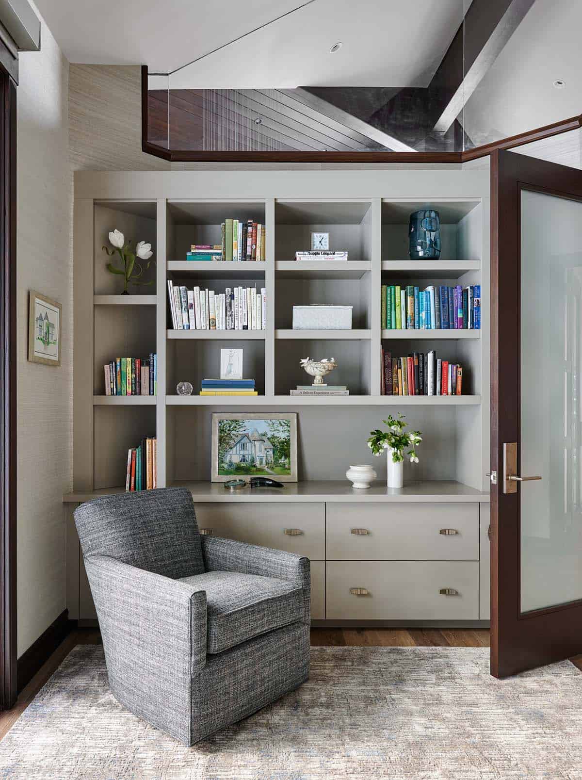Built-in bookshelf and desk nook with gray swivel chair and glass-railed loft above