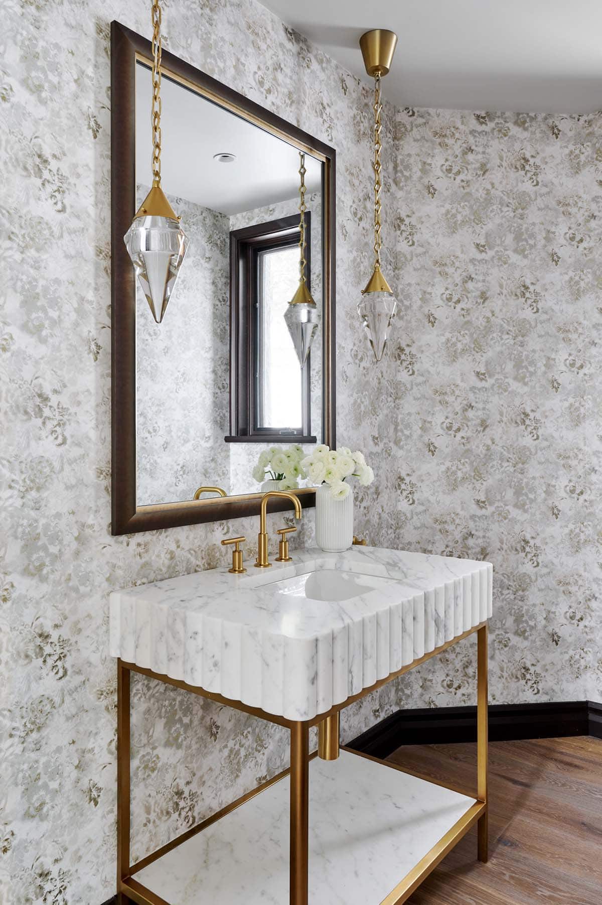 Powder room with floral wallpaper, fluted marble vanity, and brass pendant lights