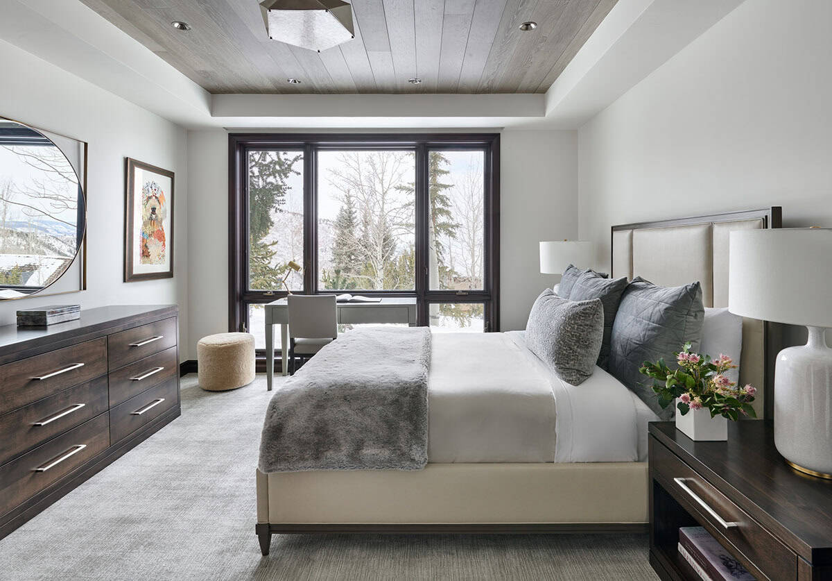 Bedroom with upholstered bed, wood ceiling, and large window overlooking snowy trees