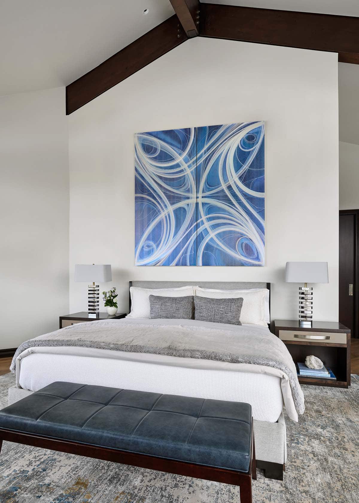 Bedroom with vaulted wood-beamed ceiling and large blue abstract artwork above bed