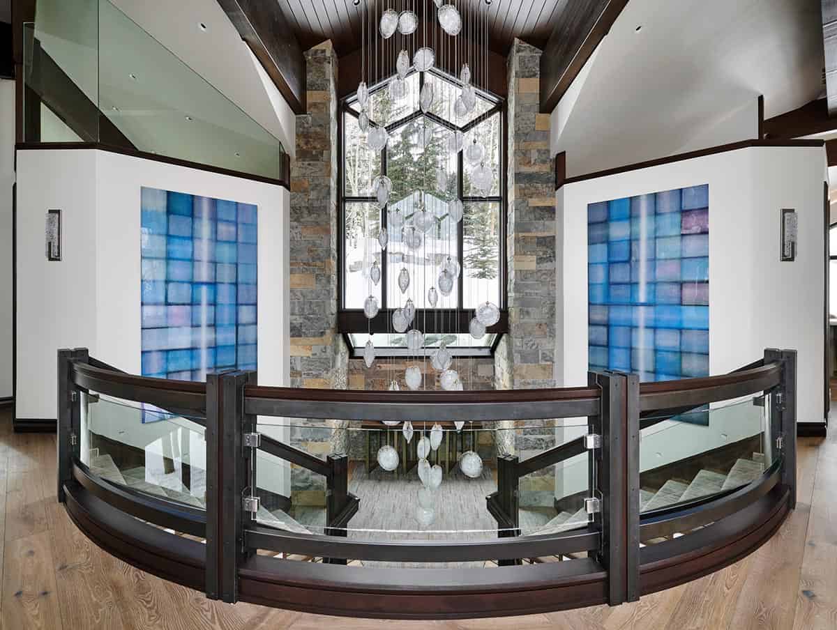 Stairwell landing with glass railing, blue tile art, and hanging glass pendant chandelier