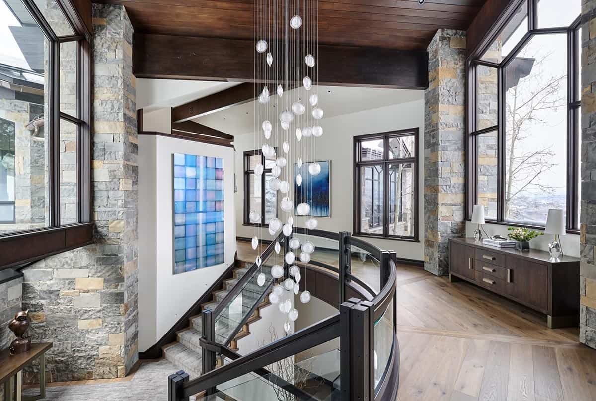 Staircase with glass balustrade, stone columns, and cascading glass pendant light