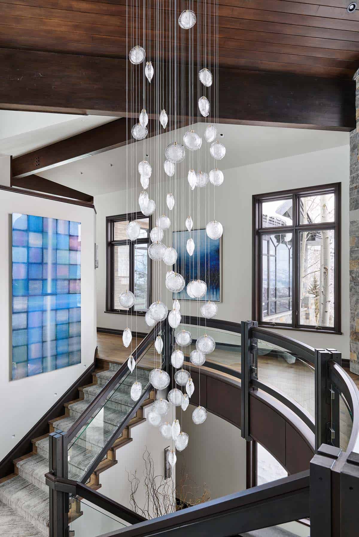 Stairwell with cascading glass pendant chandelier, glass railing, and blue tile artwork