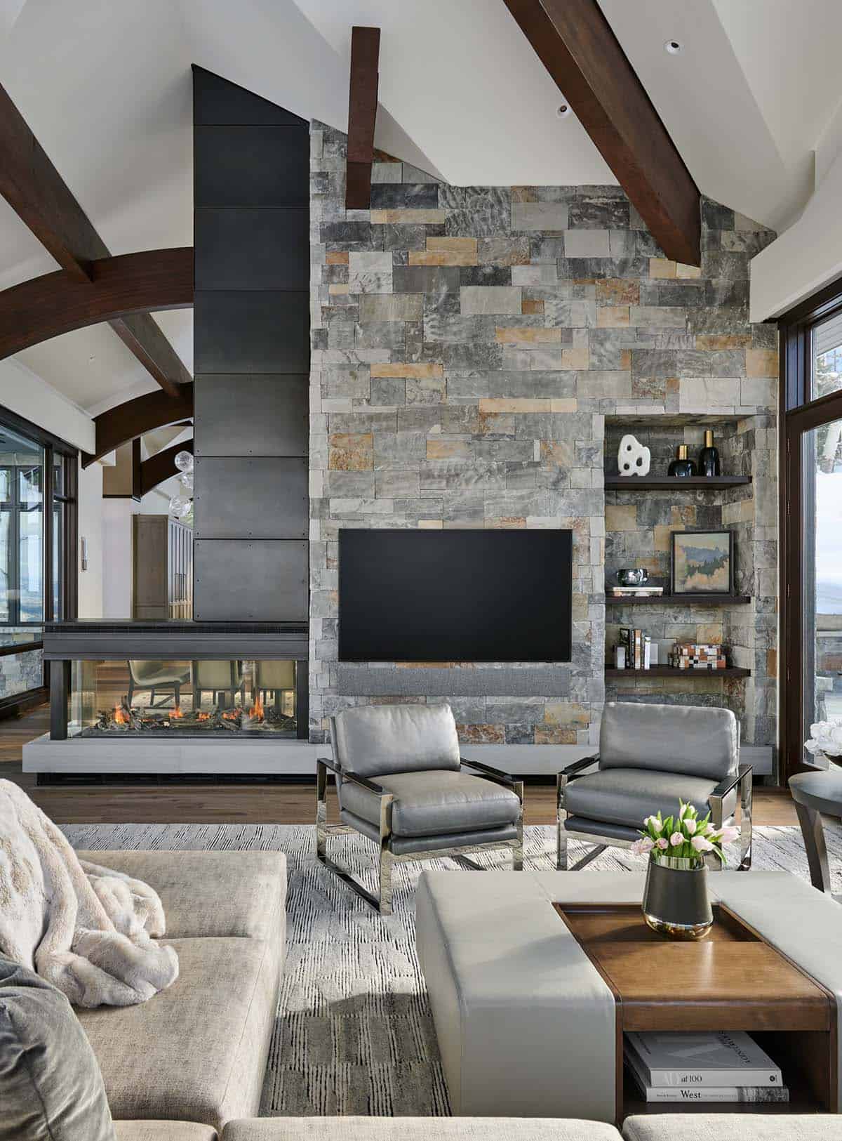 Living room with double-sided stone fireplace, TV, and gray leather chairs