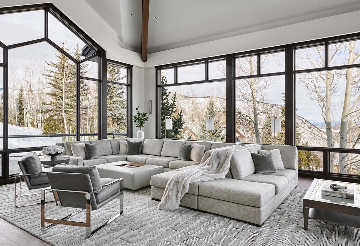 Living room sectional sofa facing floor-to-ceiling windows with mountain and forest views