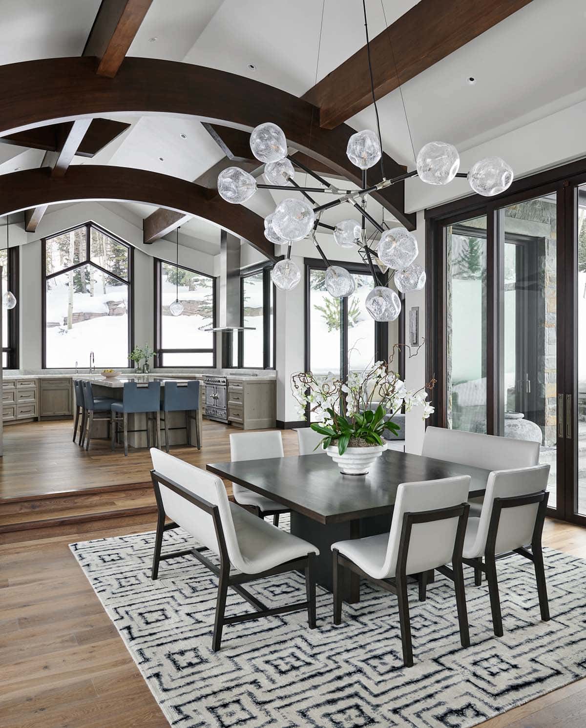 Open-concept dining and kitchen area under curved wood beams and glass-orb lighting
